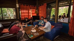 Eine Gruppe von Personen sitzt auf einer Couch und einem Tisch mit Snacks und Karten in einem Raum mit Holzwänden und großen Fenstern.