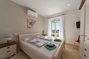 A bedroom with a bed, bedside tables, a TV, a window with curtains, and a painting on the wall. - Villa di Sogno - Montecristo Apartment (Capoliveri)