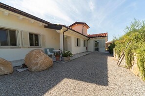 A building with a gravel driveway, a patio with outdoor furniture, and large rocks. - Villa di Sogno - Montecristo Apartment (Capoliveri)