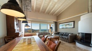 A spacious living area with a large wooden dining table, leather chairs, a fireplace, and a view of the mountains. - Villa di Sogno - Montecristo Apartment (Capoliveri)