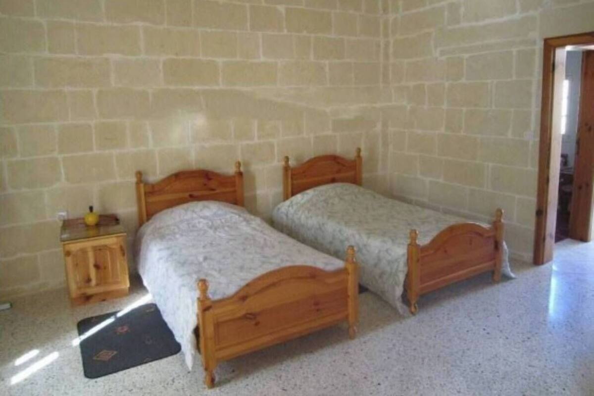 A room with two wooden beds, a small wooden nightstand, and a door leading to another room.