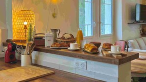 A kitchen with a wooden countertop, a coffee maker, a kettle, a basket of bread, and a bottle of orange juice. - Villa Mifa 5 minutes from the center with Lagoon Pool (Sarlat-la-Canéda)