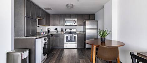 A modern kitchen with dark cabinets, stainless steel appliances, a built-in oven, and a dining area with a round table and chairs.