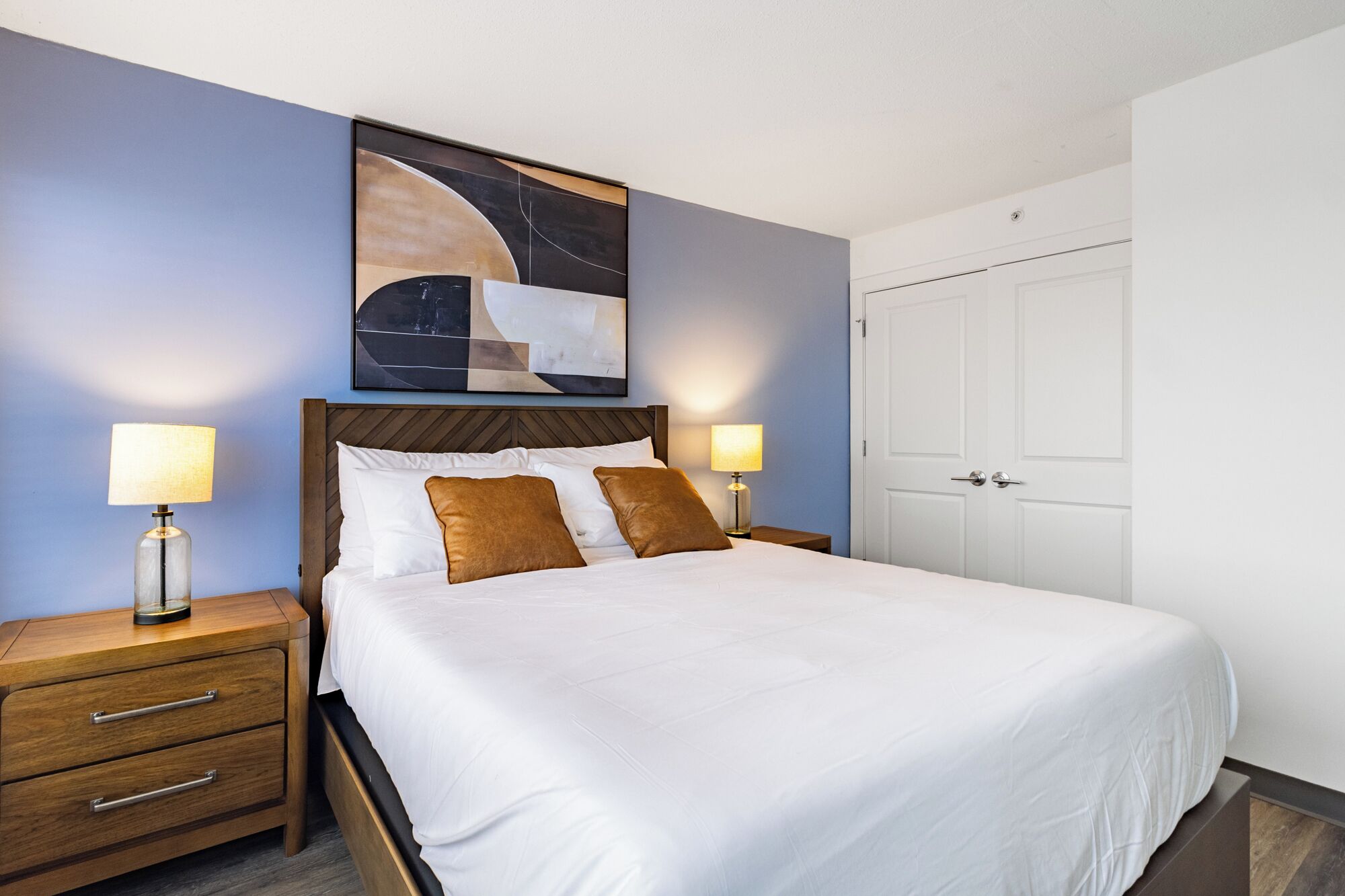 Habitación de hotel con una cama grande, dos mesitas de noche, un cabecero de madera y un cuadro sobre la cama.