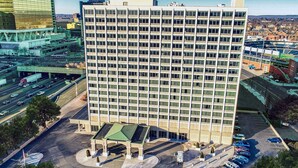 Korkea hotellirakennus, jossa on suuri määrä ikkunoita rivissä, parkkipaikka ja viherkatolla varustettu sisäänkäynti.