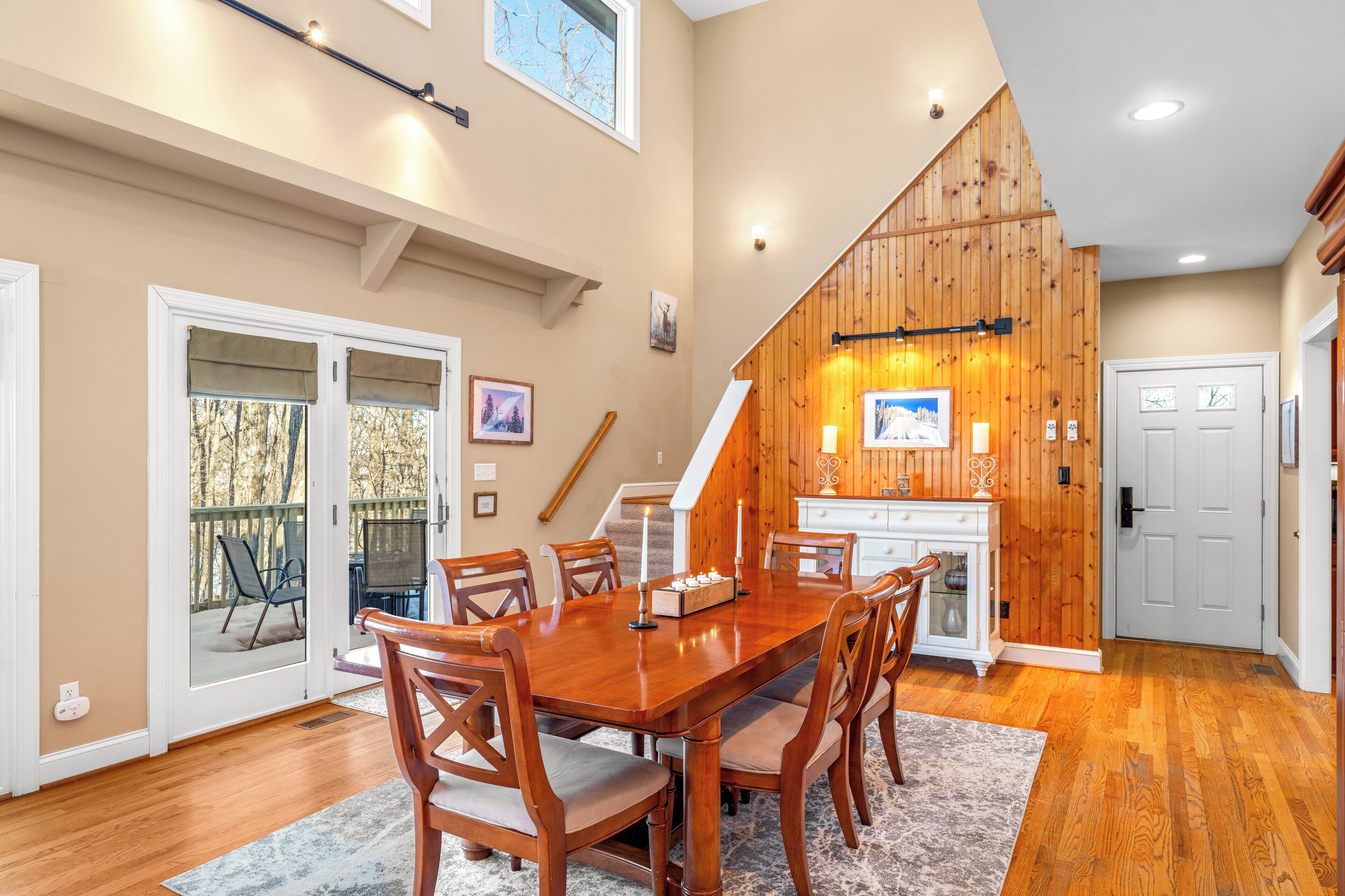 A dining area with a wooden table and chairs, a staircase, and a kitchen area with wooden walls.
