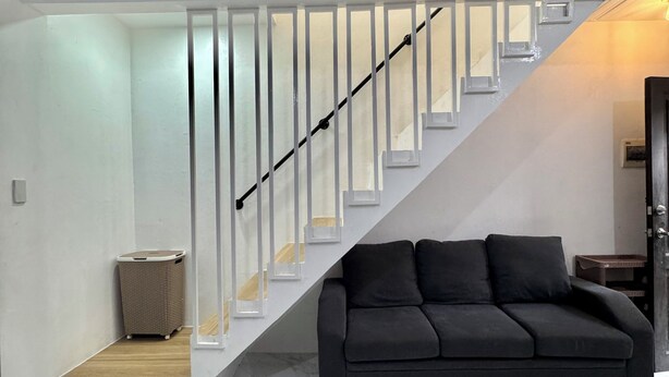 A modern living room with a black sofa, a staircase with white railings, and a marble floor.