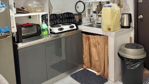 A compact kitchen with a microwave, toaster, and gas stove. There are shelves with kitchenware and a trash bin.