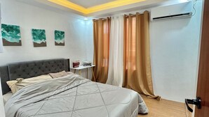 A bedroom with a bed, a bedside table, a wall-mounted air conditioner, and a ceiling light fixture.
