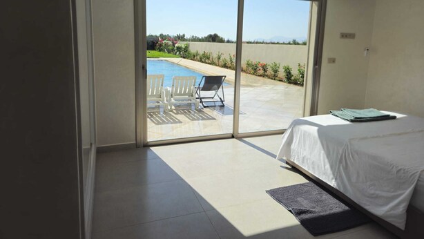 A bedroom with a bed, a view of a swimming pool, and a patio area with chairs and a table. - Villa in Berkane with swimming pool, not overlooked (Berkane)