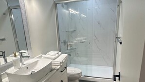 Une salle de bain moderne avec un grand miroir, un lavabo blanc et une cabine de douche en verre.