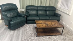 Un salon avec un canapé en cuir vert foncé, un fauteuil assorti et une table basse en bois.