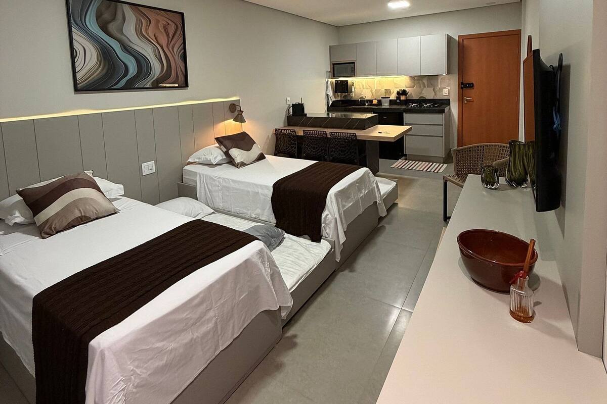 A hotel room with two beds, a kitchenette, a flat-screen TV, and a painting on the wall.