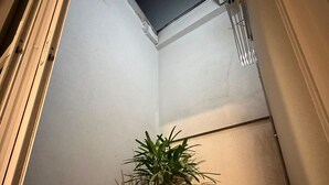 Un passadís estret amb una planta en test, una reixa de ventilació i un marc de porta.