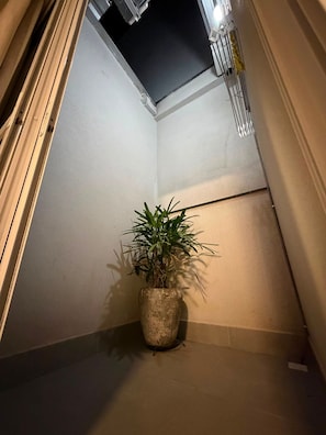 A narrow hallway with a potted plant, a ceiling vent, and a door frame. - Tc Loft (Uberlândia)
