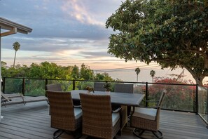 Eine Terrasse mit Korbmöbeln, einem Tisch und Stühlen, mit Blick auf einen Garten mit Bäumen und den Himmel.