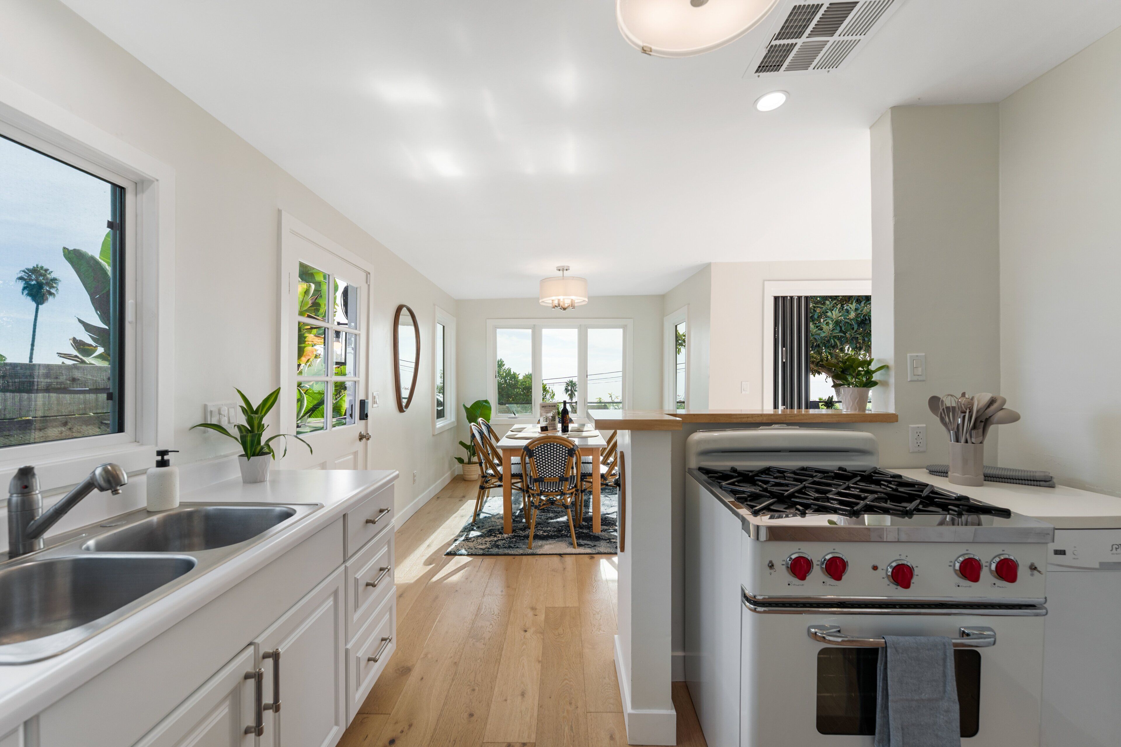 Una cocina moderna con armarios blancos, estufa a gas y un comedor con mesa y sillas de madera.