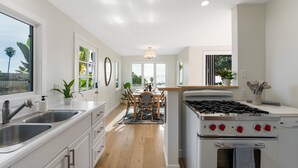 A modern kitchen with white cabinetry, a gas stove, and a dining area with a wooden table and chairs. - Ocean-View Wellness Home | Infrared Sauna + Spa (Summerland)