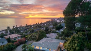 A residential area with houses, trees, and a sunset over the water. - Ocean-View Wellness Home | Infrared Sauna + Spa (Summerland)