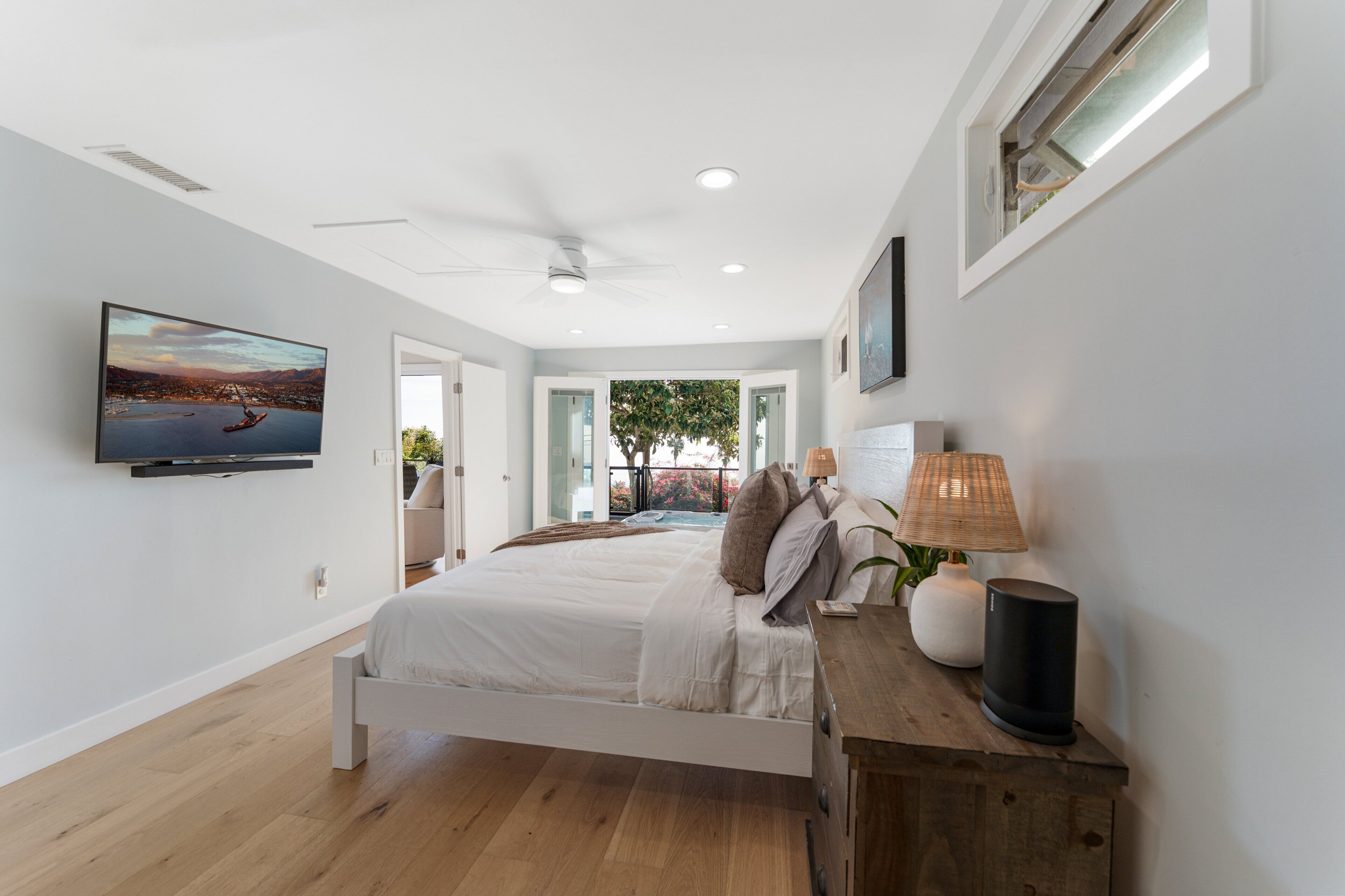 Un dormitorio moderno con una cama, un televisor, un ventilador de techo y vistas al exterior.