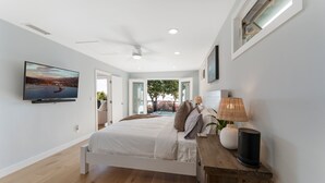 A modern bedroom with a bed, a television, a ceiling fan, and a view of the outdoors. - Ocean-View Wellness Home | Infrared Sauna + Spa (Summerland)