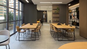Een moderne vergaderruimte met grote ramen, twee lange tafels met stoelen en een decoratieve boekenkast met planten.