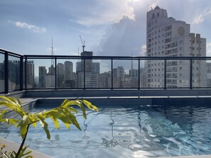Piscina no terraço com vista para a cidade, rodeada por um guarda-corpo de vidro.