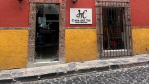 A building with a red and yellow facade, a sign for 'Casa del Tio Hotel Boutique', and a cobblestone street in front. - Casa del Tio Hotel Boutique (San Miguel de Allende)