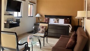 A cozy room with a wooden ceiling, a bed with a headboard, a sofa, a chair, a TV, and a small table. - Casa del Tio Hotel Boutique (San Miguel de Allende)