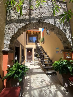 A stone archway leading to a staircase with a view of a building. There are potted plants and a bench. - Casa del Tio Hotel Boutique (San Miguel de Allende)