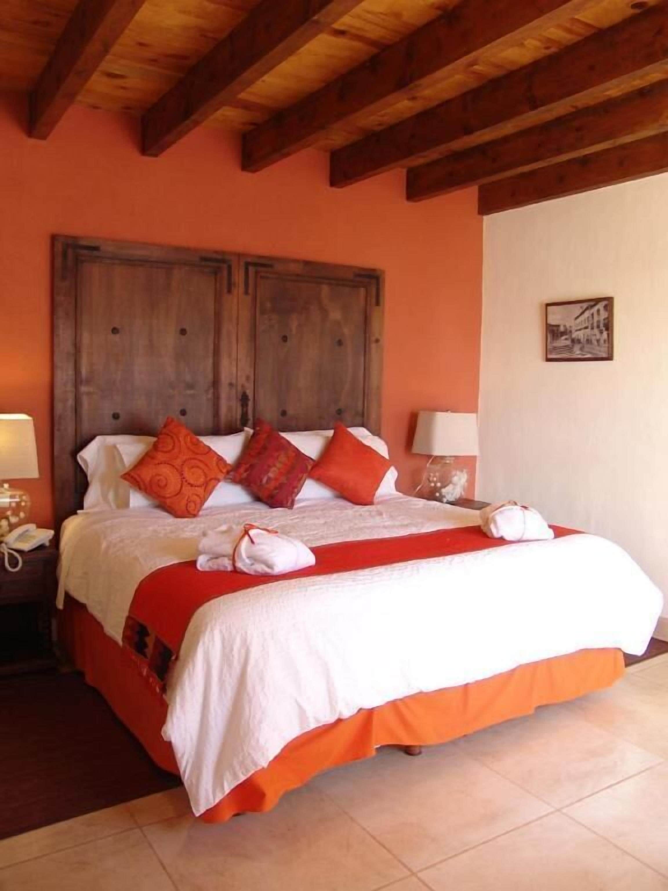 A bed with a wooden headboard, white and orange bedding, and red pillows.