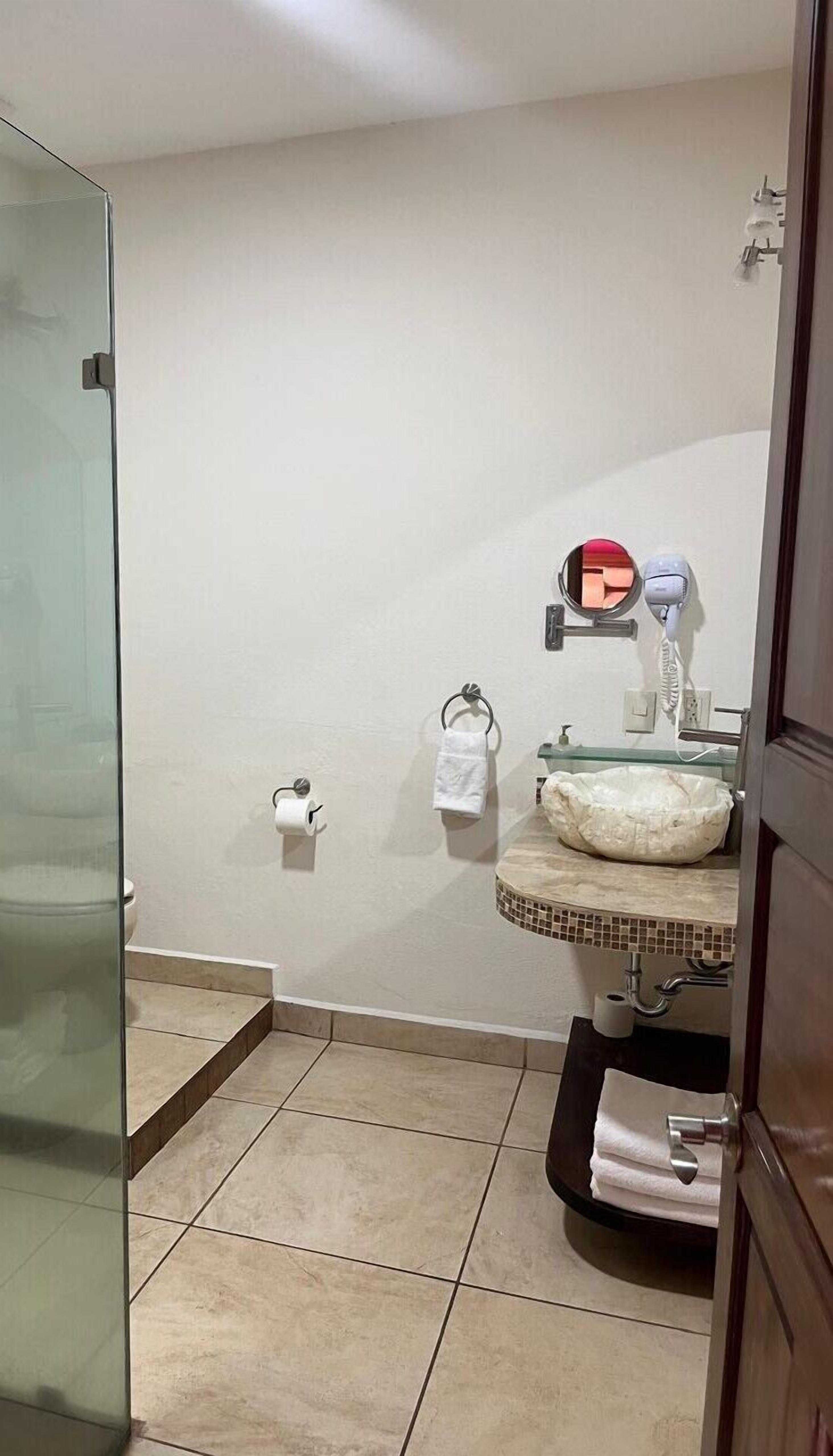 A bathroom with a glass shower door, a sink with a mirror, and two rolls of toilet paper on the wall.