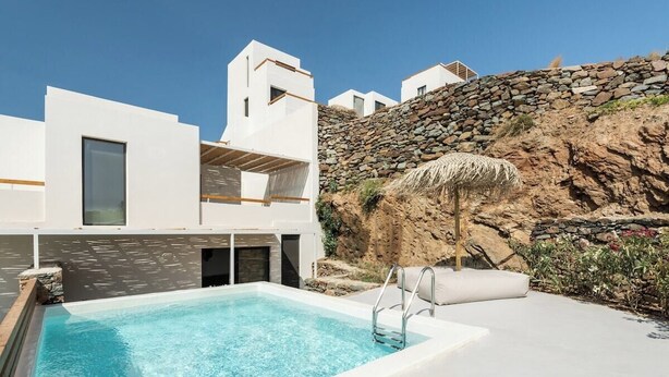 A modern pool area with a clear blue pool, white buildings, and a stone wall. - Boutique Villa Ciel Tinos (Tinos)