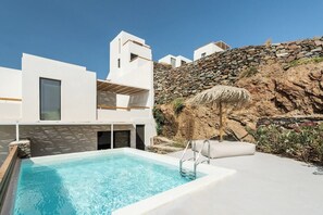 A modern pool area with a clear blue pool, white buildings, and a stone wall. - Boutique Villa Ciel Tinos (Tinos)