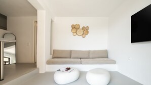 A modern living room with a sofa, two white ottomans, a wall-mounted TV, and a decorative wall piece. - Boutique Villa Ciel Tinos (Tinos)