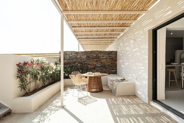 A modern outdoor patio with a stone wall, a round table, and wicker chairs. - Boutique Villa Ciel Tinos (Tinos)
