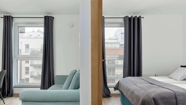 Een moderne hotelkamer met een groot raam, een bank, een bed en een houten vloer.