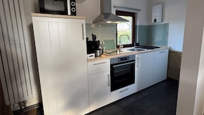 Une cuisine moderne avec des meubles blancs, un four encastré, un micro-ondes et une fenêtre donnant sur un espace verdoyant.