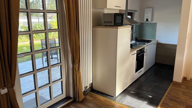 Une cuisine moderne équipée d’un four à micro-ondes, d’un four et d’un évier intégrés. Une porte-fenêtre coulissante donne accès à un espace patio.