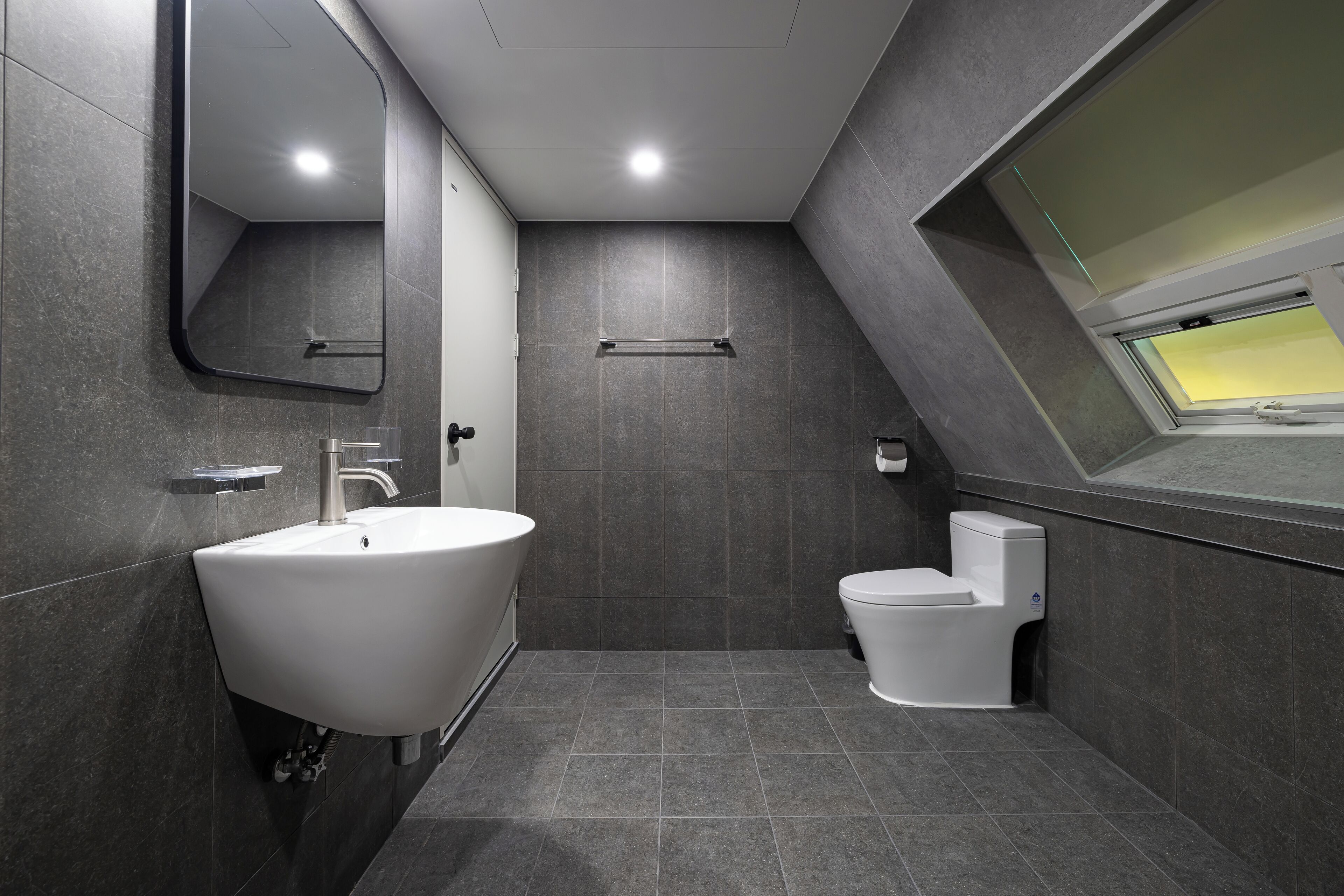 A modern bathroom with a large sink, toilet, and a skylight.