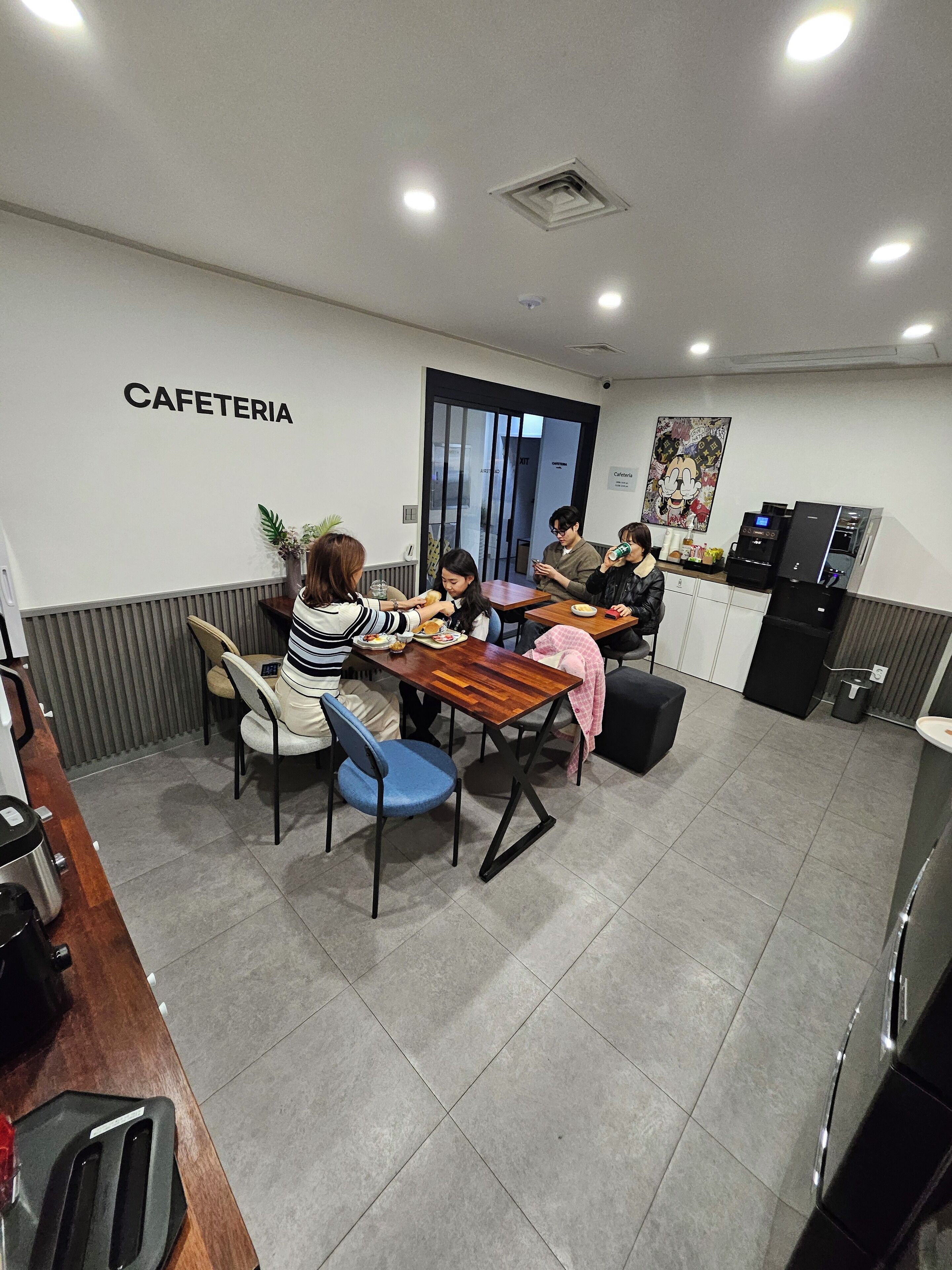 A cafeteria with a sign on the wall, several tables, chairs, and a coffee machine.