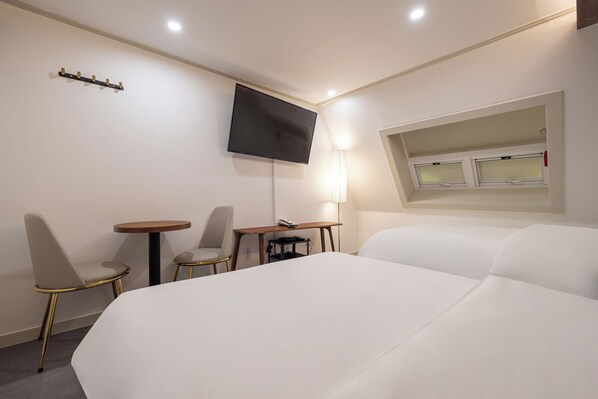 Une chambre d’hôtel avec un grand lit, un bureau avec une chaise, un téléviseur fixé au mur et une fenêtre avec des stores.