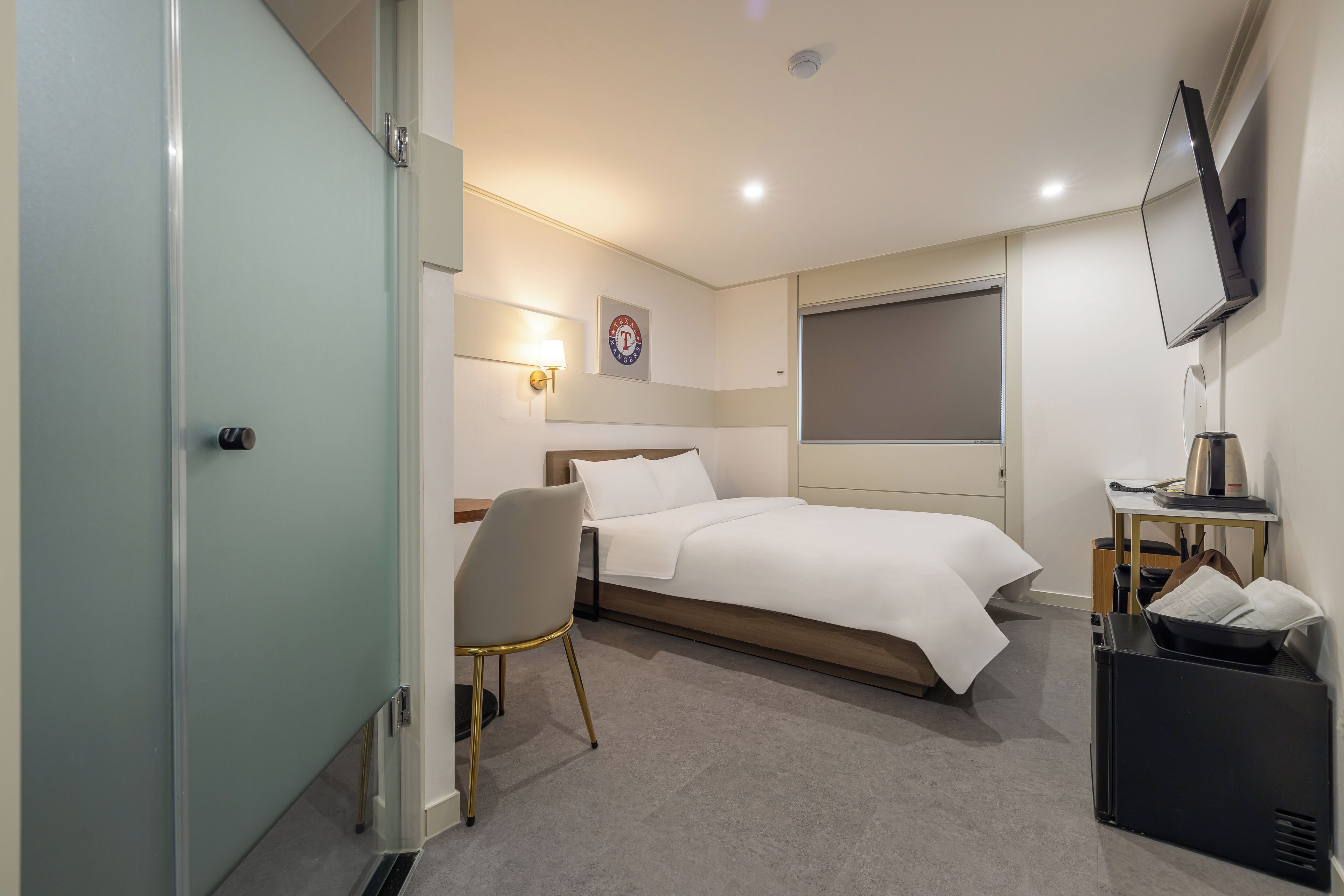 Una habitación de hotel moderna con una cama, un escritorio, una silla, un televisor y un reloj en la pared.