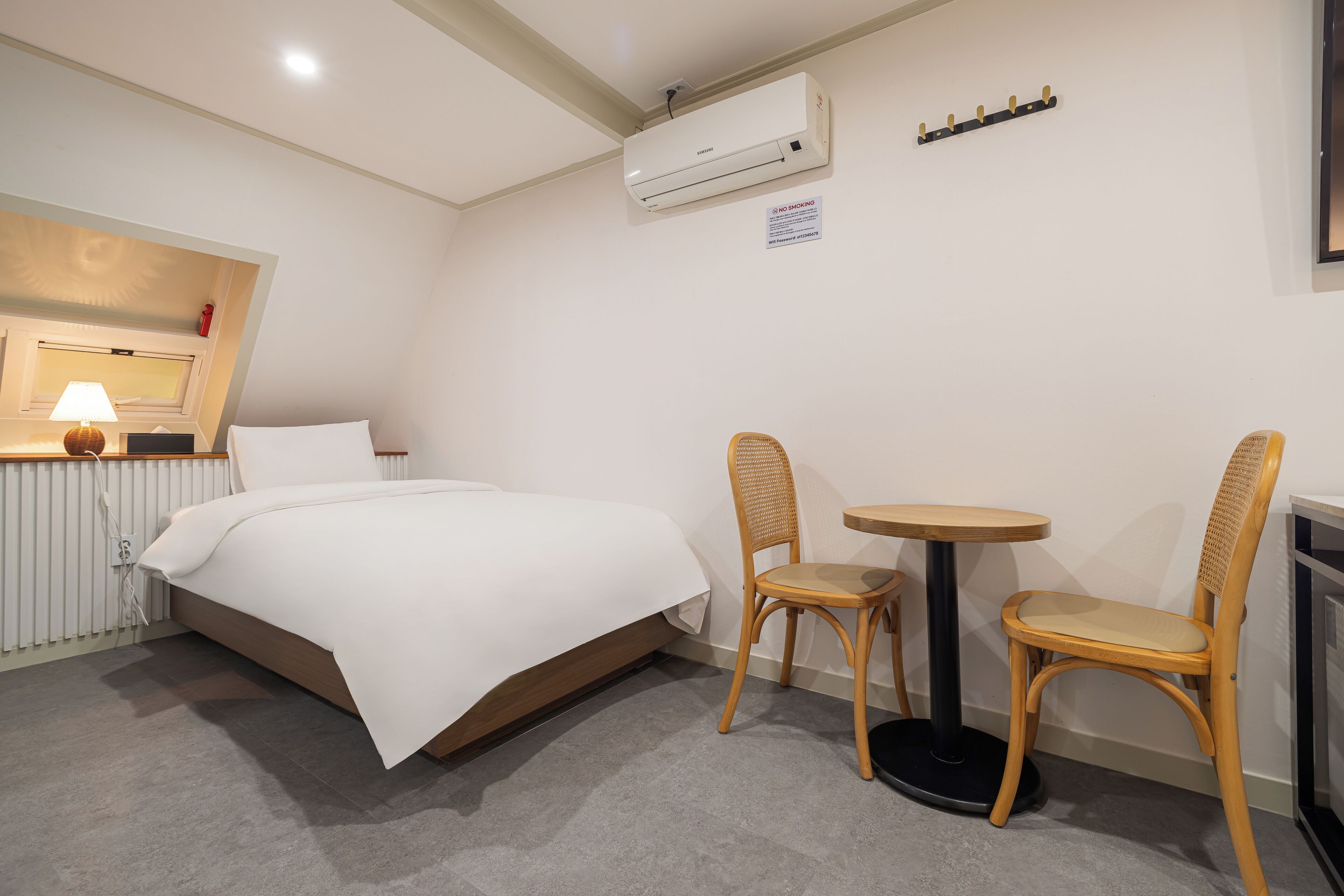 Habitación de hotel con cama, dos sillas, una mesita, un equipo de aire acondicionado, una lámpara y un radiador.
