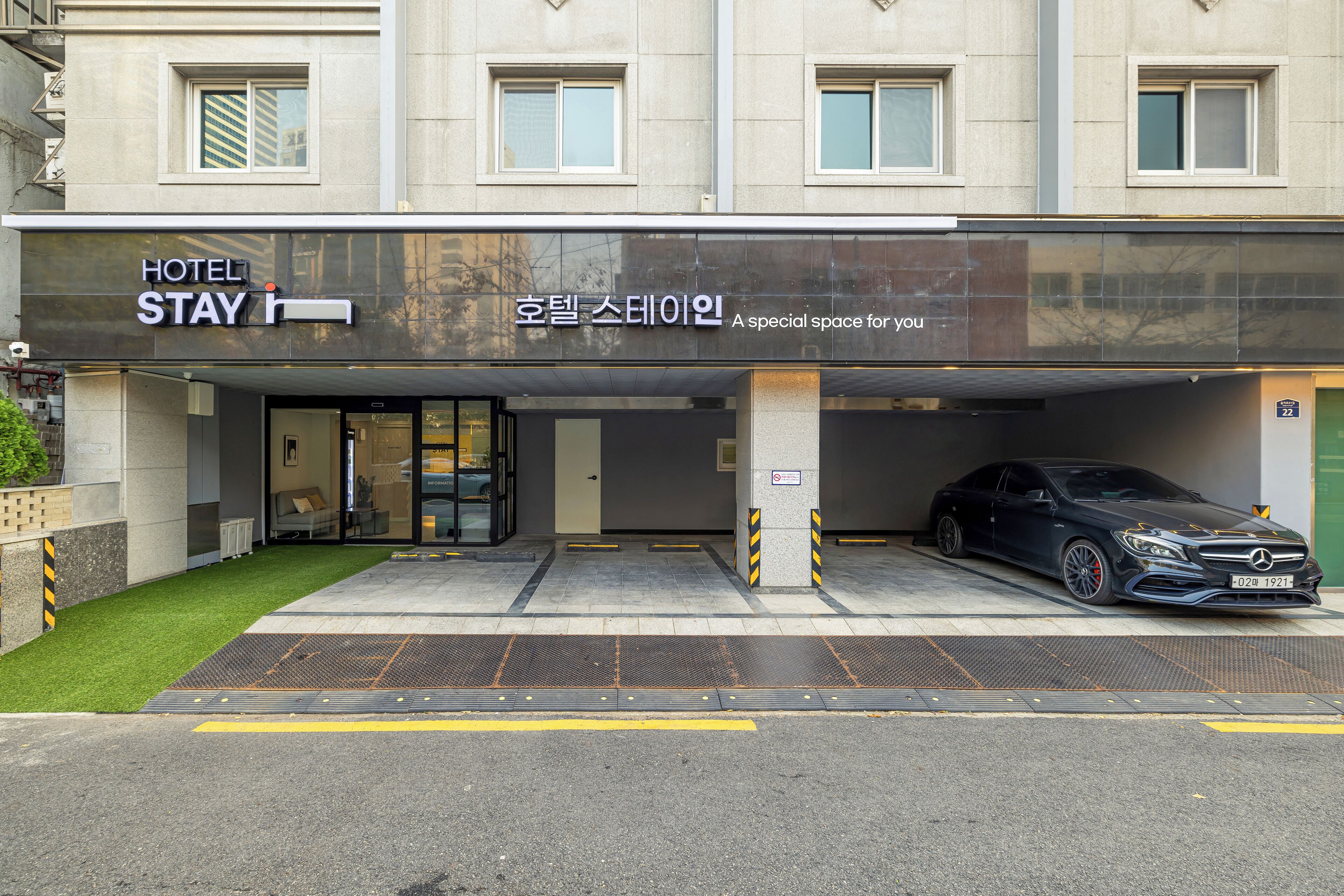 A hotel entrance with a black awning, a Mercedes-Benz parked in the garage, and a sign in Korean.