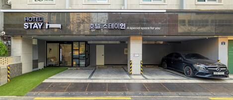 A hotel entrance with a black awning, a Mercedes-Benz parked in the garage, and a sign in Korean.