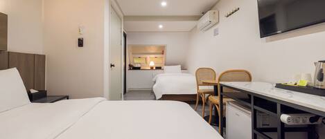 Habitación de hotel con cama, escritorio, silla, televisor y kitchenette.