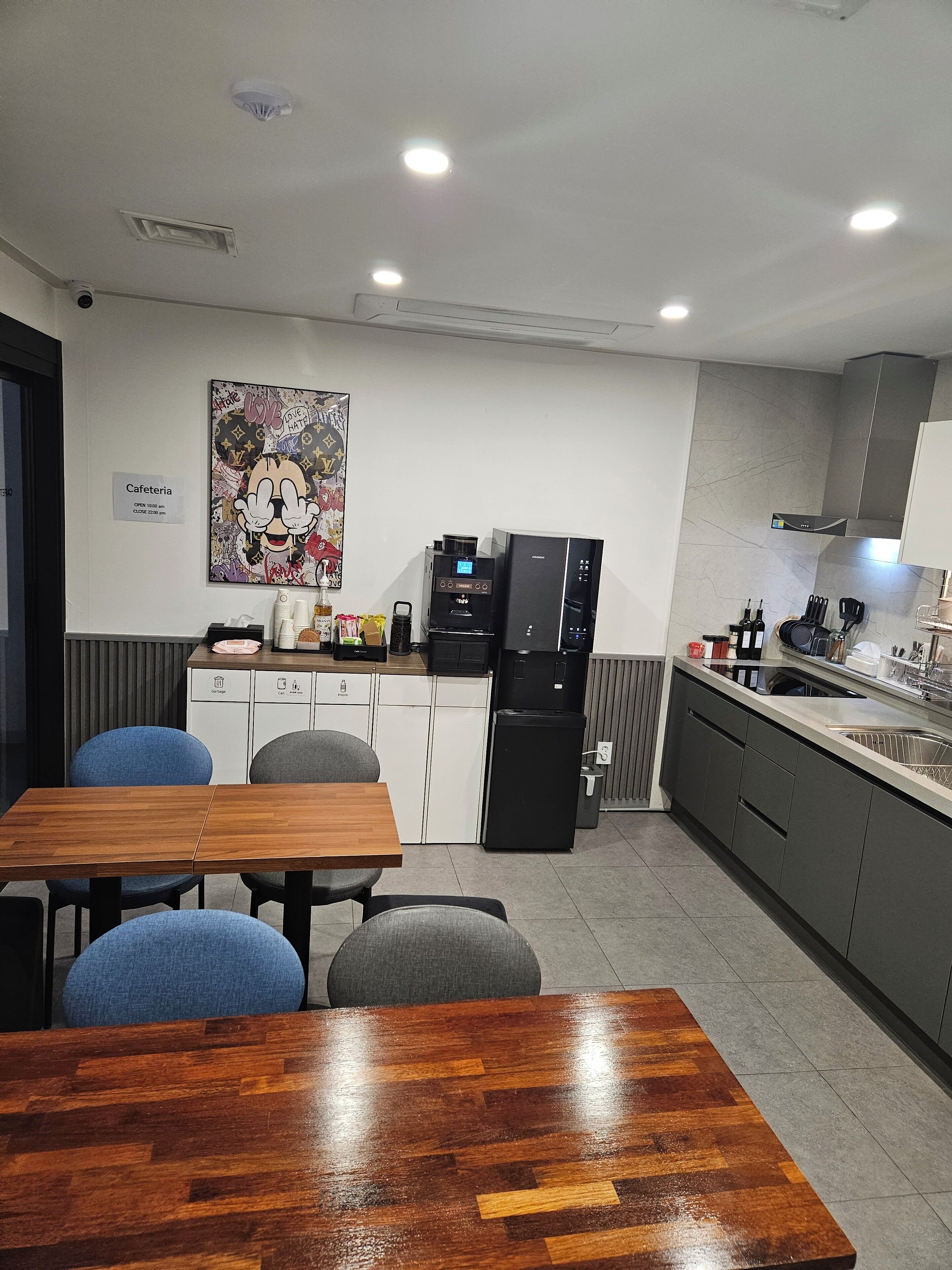 Una cuina moderna amb cafetera, nevera i zona de menjador amb taula i cadires de fusta.