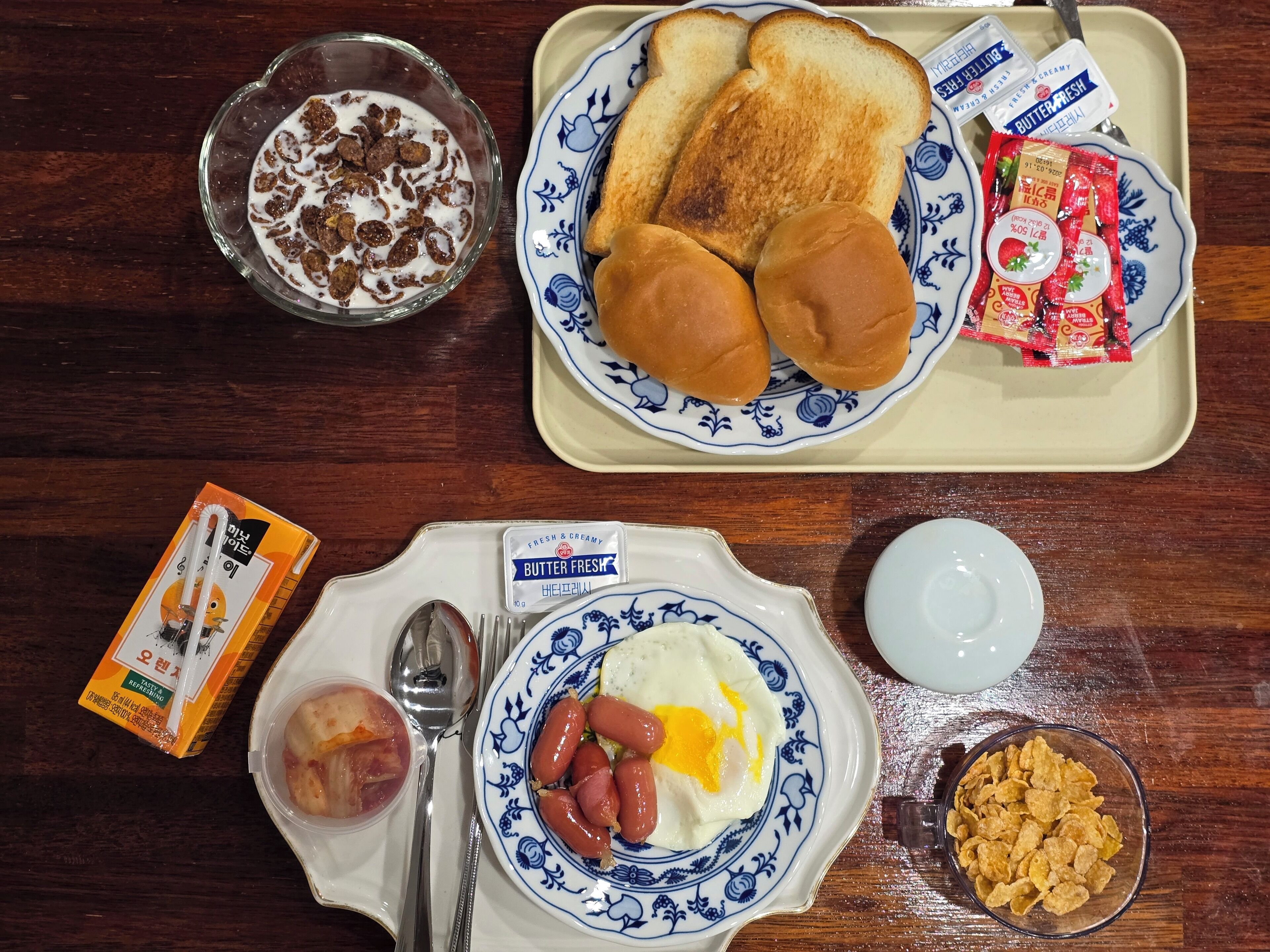 A breakfast tray with toast, butter, jam, cereal, and a plate with eggs and sausages.