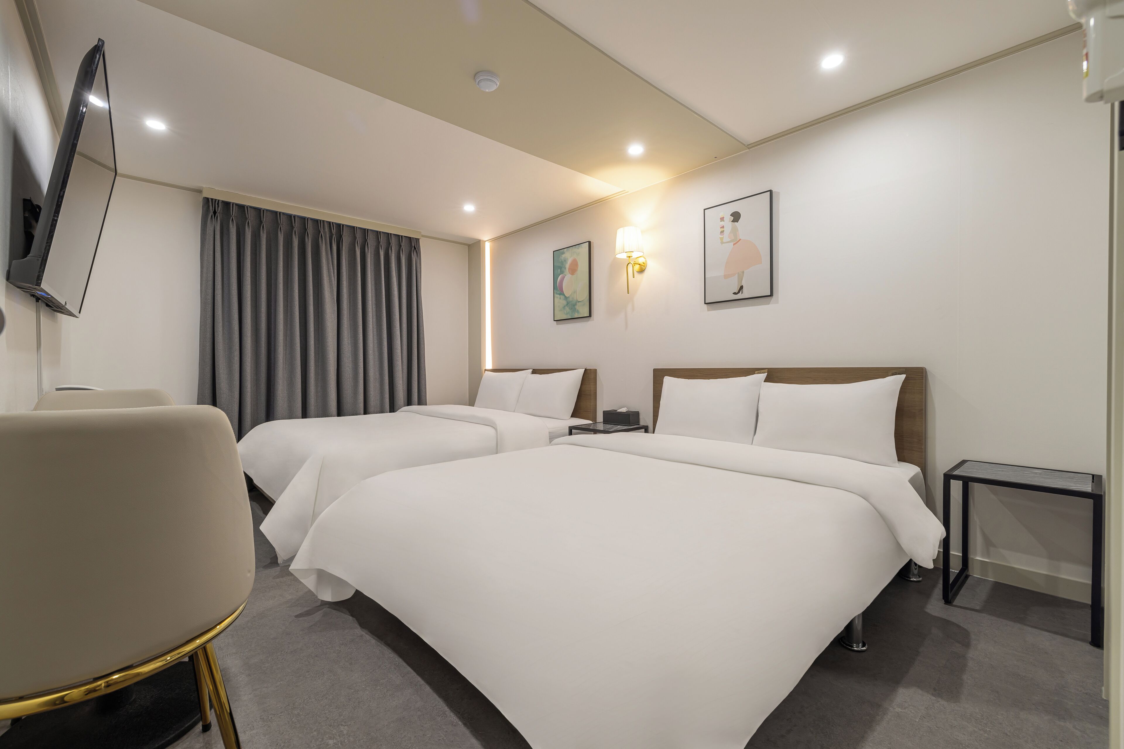 Ein Hotelzimmer mit zwei Betten, einem Flachbildfernseher an der Wand, einem Schreibtisch und einem Stuhl.